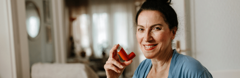 Smiling older woman holding asthma inhaler at home
