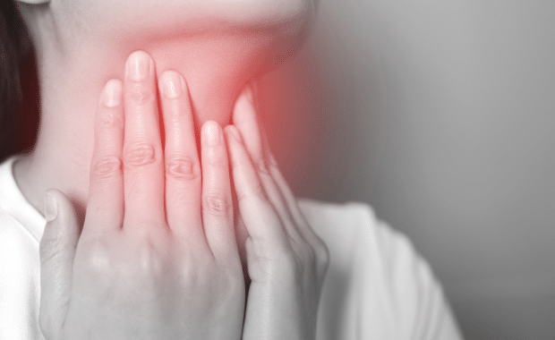 sore throat pain. Closeup of young woman sick holding her inflamed throat using hands to touch the ill neck in blue shirt on gray background.