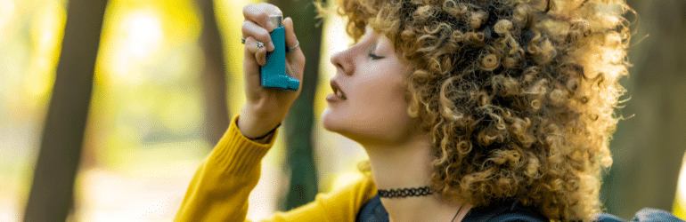 Woman hiker using inhaler outside in woods .Young woman treating asthma with inhaler