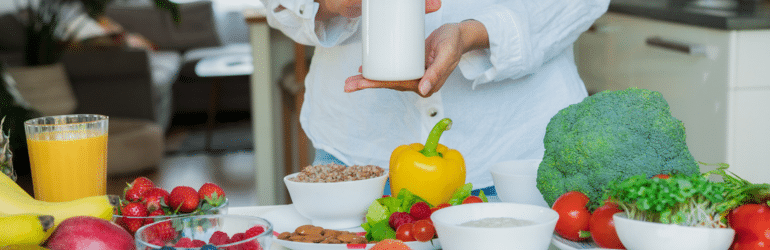 Focus on female hand holding white mockup jar with nutritional supplements on table with fresh food ingredients. Concept of Balanced Diet. Supplementing diet with missing vitamins. Dietary supplement.